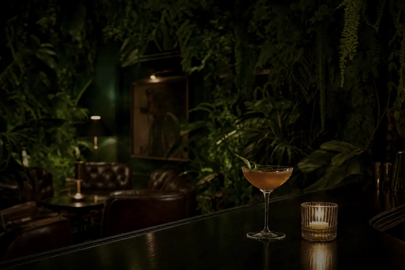 The Flora Room — a hidden speakeasy below Porzana, lush with green plants on leaf-green walls, a single cocktail glowing on the dark bar.