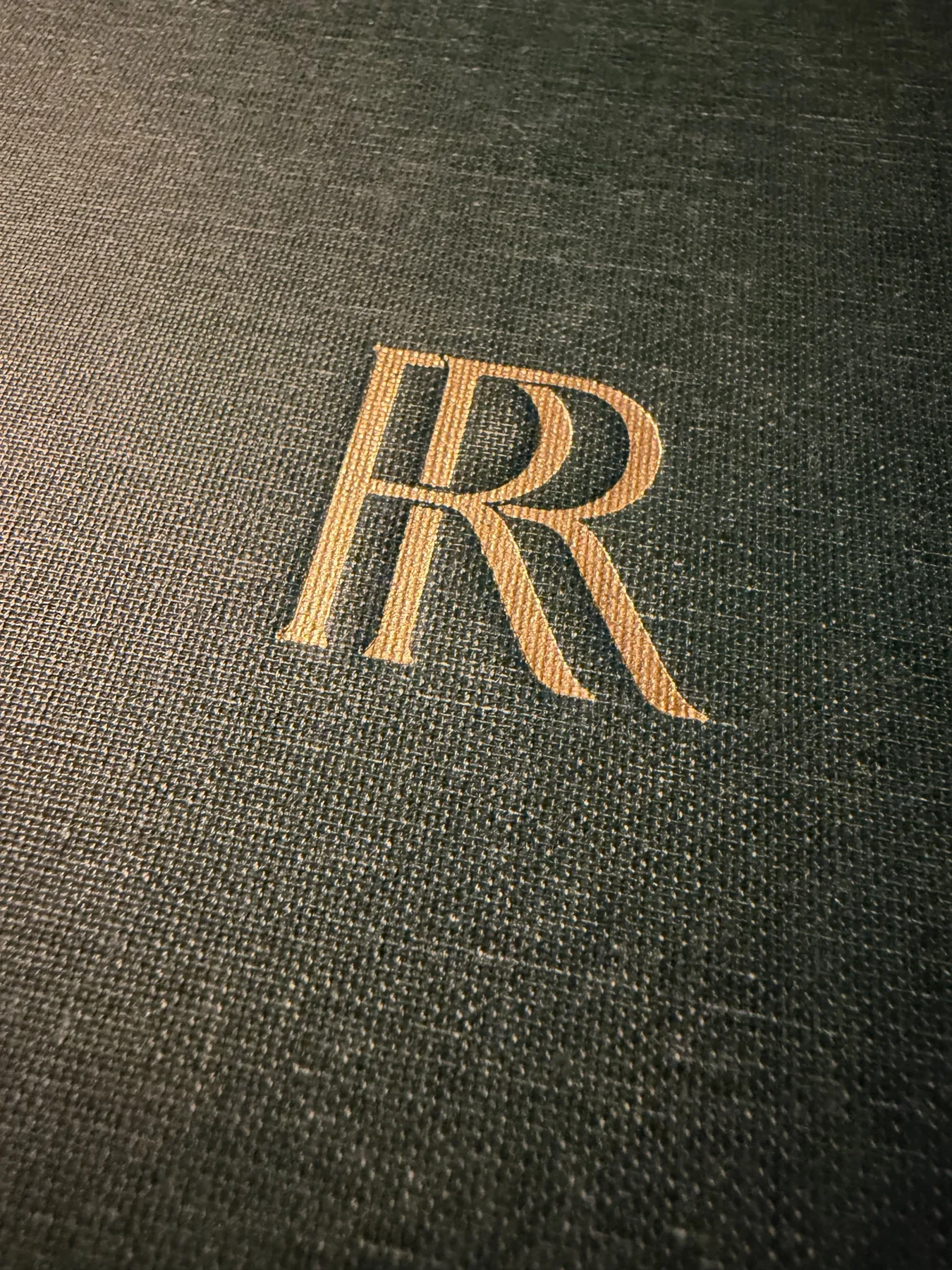 The Robin Room menu cover — gold-foil RR monogram embossed on forest-green linen.