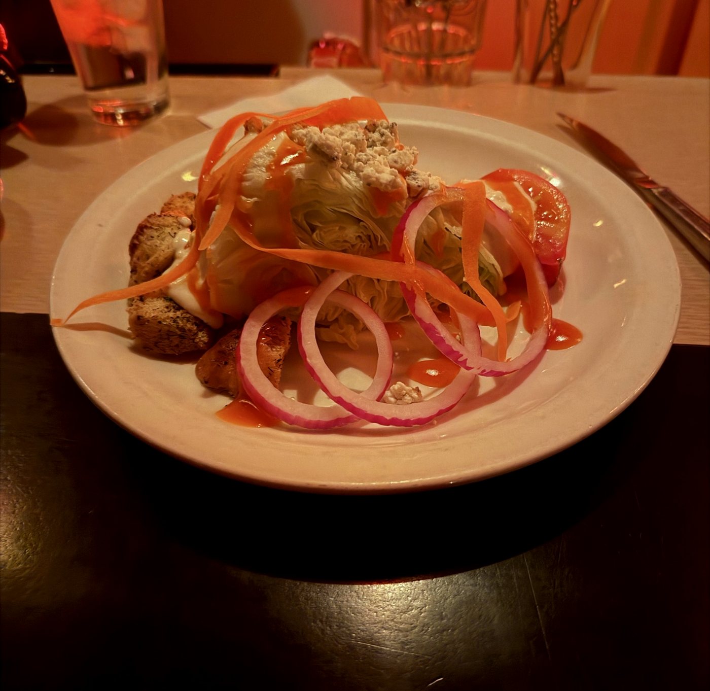 Iceberg Wedge with French-Roquefort dressing, carrot ribbons, pickled red onion, tomato wedge, and toasted bread crouton on a white plate at Tornado Steak House, Madison.